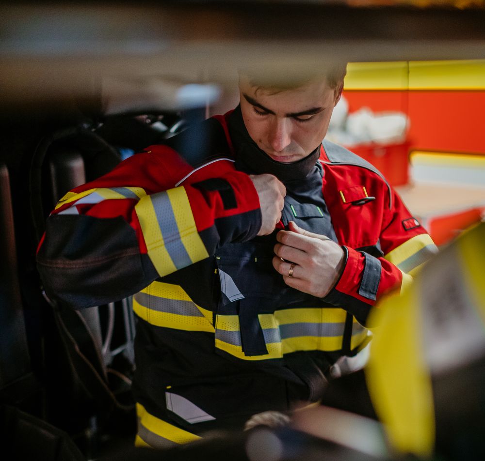 Einsatzkraft legt ihre Feuerwehrschutzjacke mit Reflexstreifen an