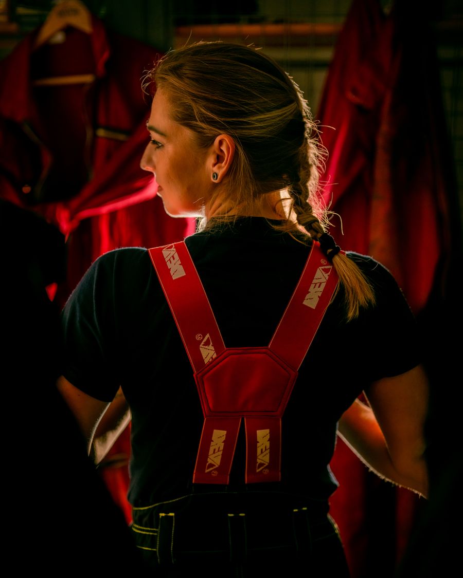 Einsatzkraft in Feuerwehr-Schutzhose mit roten Hosenträgern im Umkleidebereich