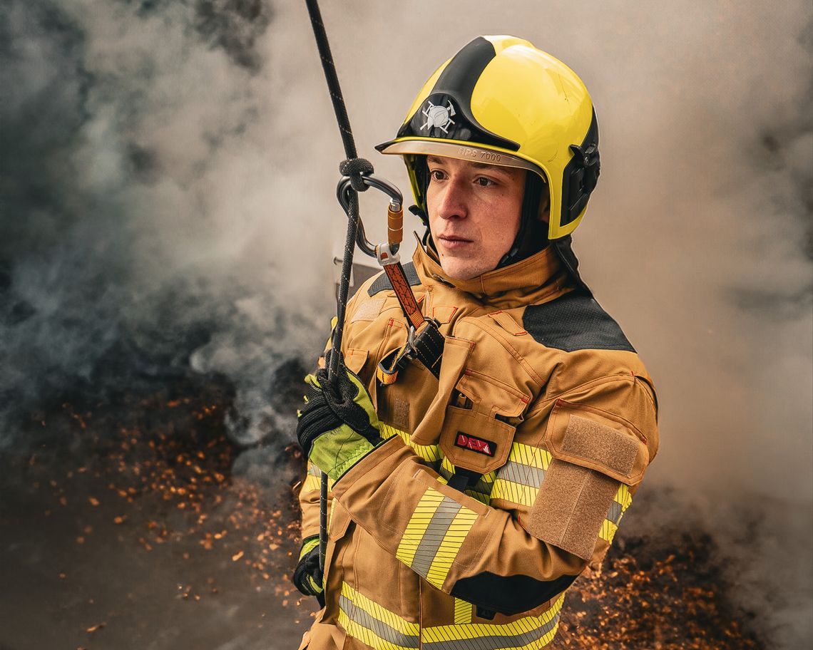 Feuerwehrmann in Schutzkleidung nach EN 469 mit Helm und Sicherungsseil im Rauch